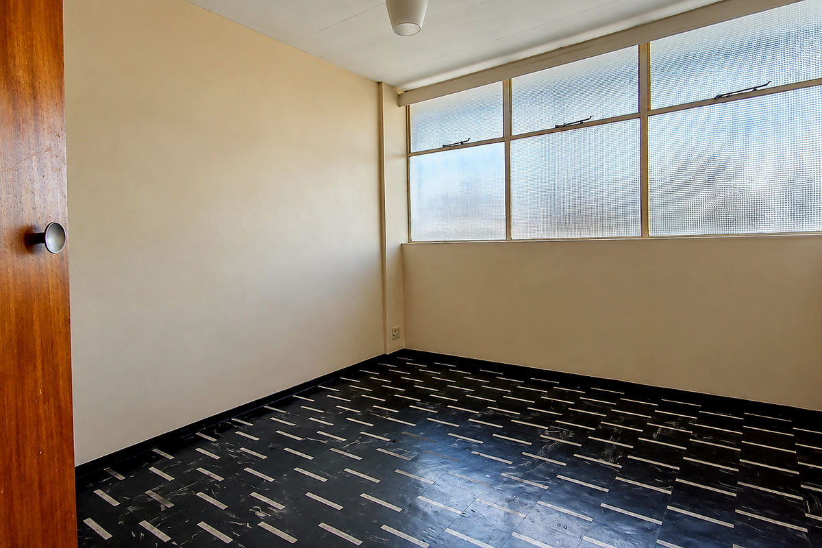 An empty bedroom featuring patterned vinyl flooring, a wooden door, and large windows with textured glass panes.