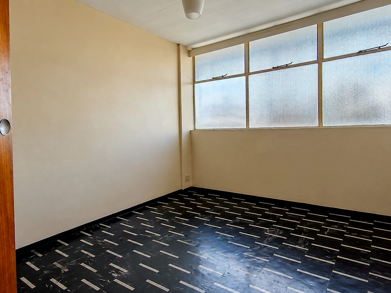 An empty bedroom featuring patterned vinyl flooring, a wooden door, and large windows with textured glass panes.