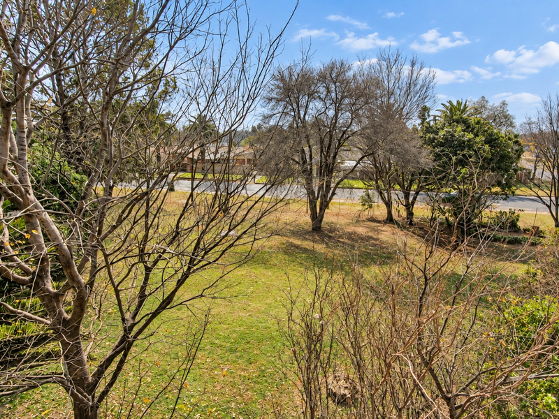 An elevated view overlooking a landscaped garden area with mature trees and a suburban street in the background.