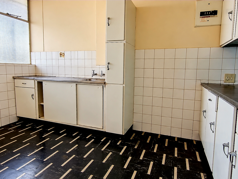 A dated, empty kitchen featuring original built-in cabinetry, tiled splashbacks, and vinyl flooring, offering a blank canvas for a modern renovation.