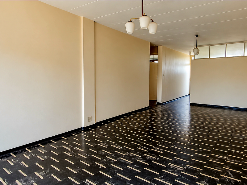 A spacious, empty living area featuring distinctive dark patterned tiled flooring, neutral walls, and classic pendant lighting fixtures.