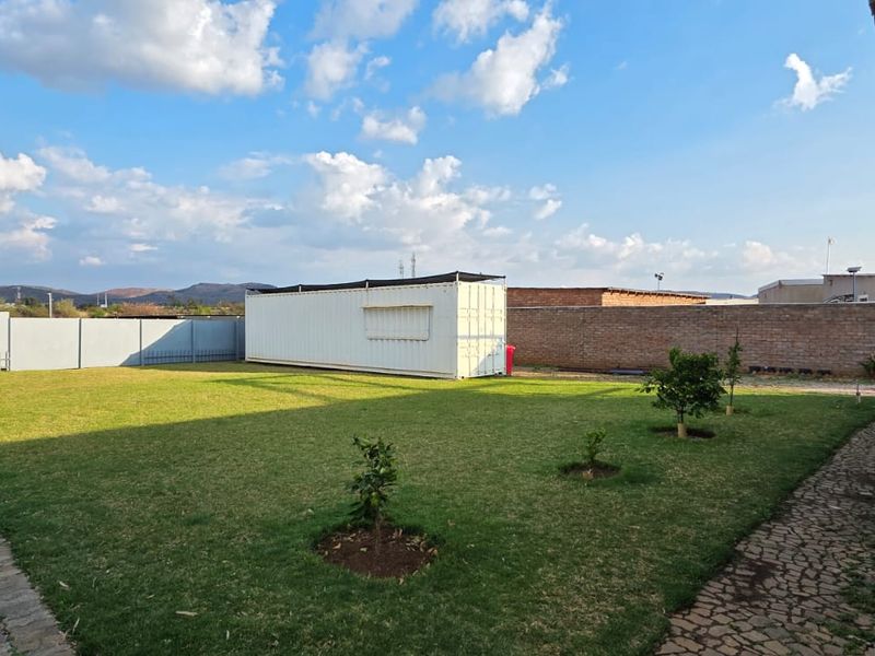 Spacious rear yard featuring a manicured lawn, paved pathways, perimeter boundary walls, and a standalone shipping container structure.