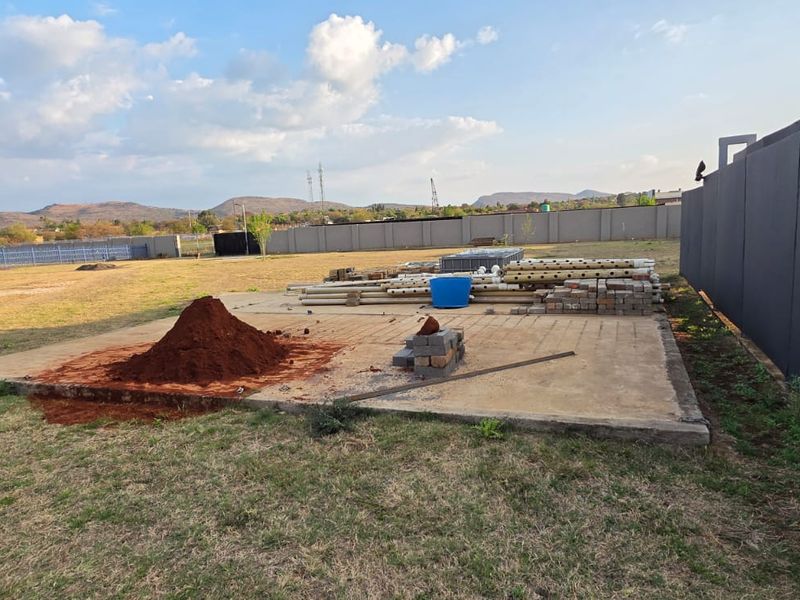 A large, open rear yard area featuring a concrete slab foundation, perimeter walling, and metal fencing, currently used for storage of construction materials.