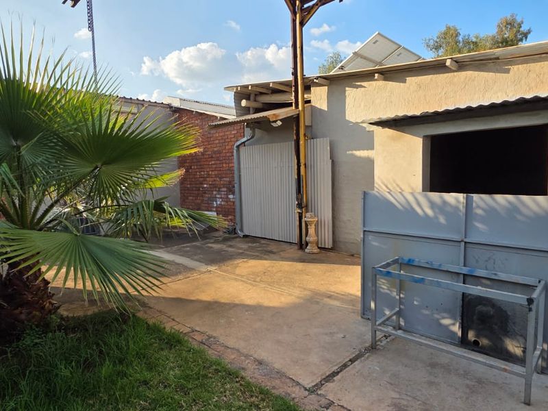 Rear exterior area featuring concrete paving, brick and metal wall finishes, and a small garden space.