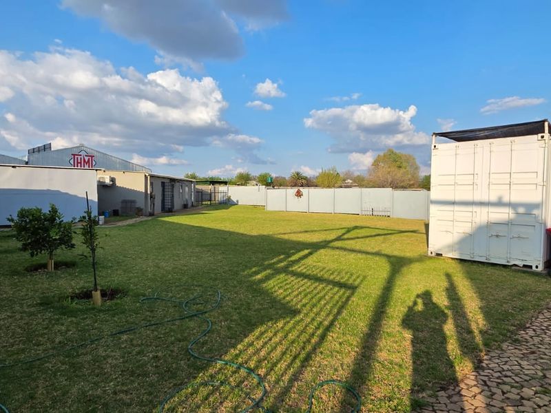 A spacious rear yard area featuring a well-maintained lawn, paved pathways, perimeter walling, and a large storage container structure.