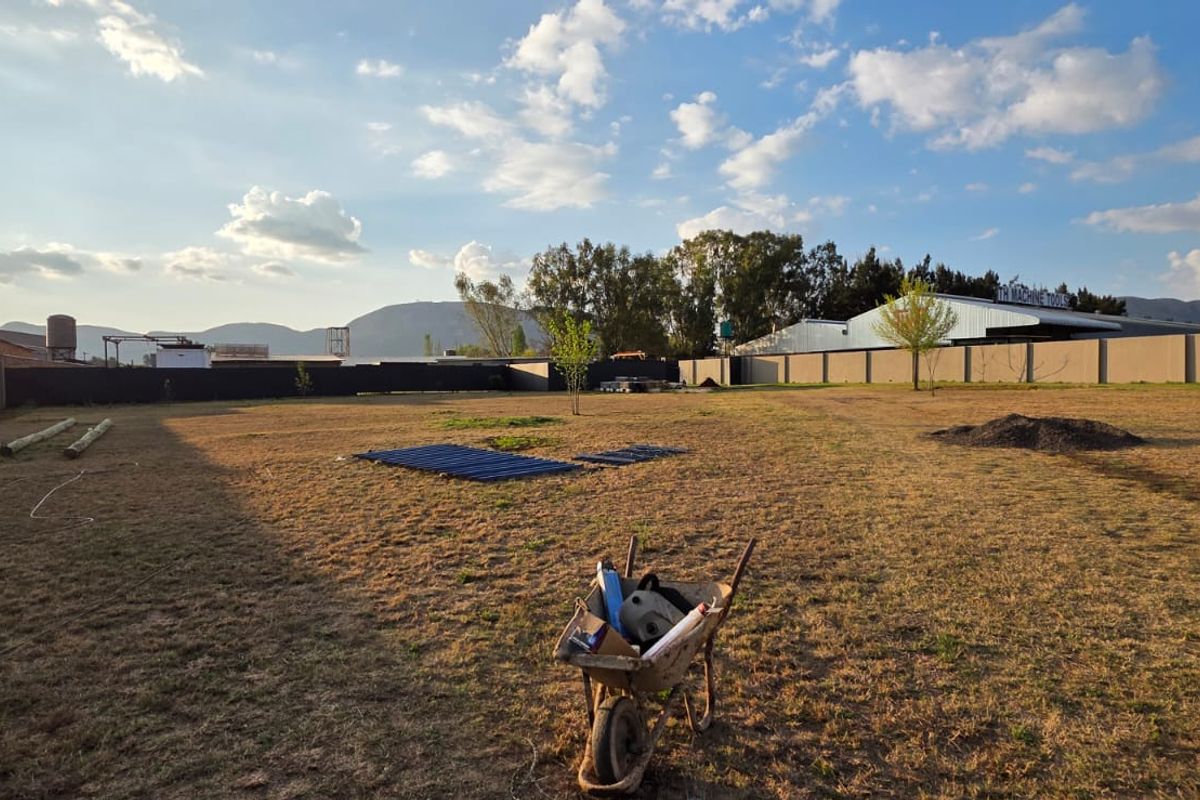 A large, open commercial plot enclosed by perimeter walls, featuring expansive grassed grounds and mountain views in the background.
