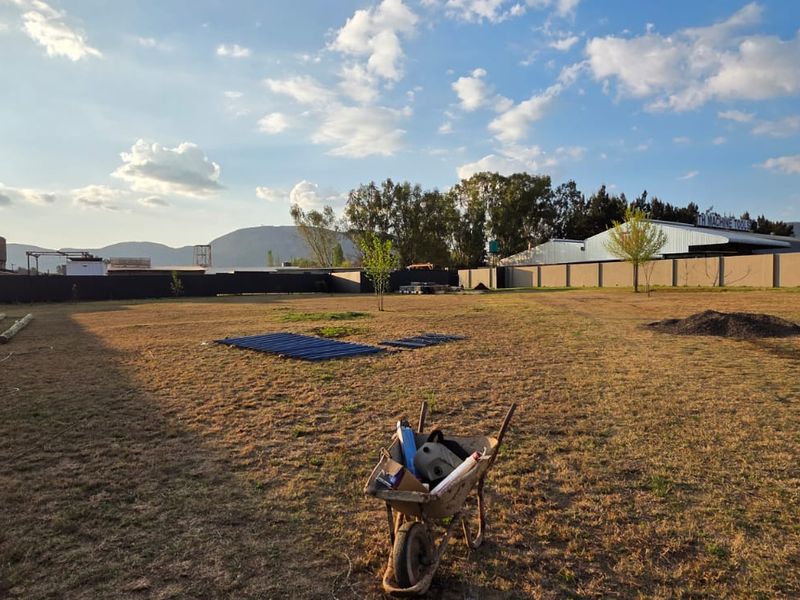 A large, open commercial plot enclosed by perimeter walls, featuring expansive grassed grounds and mountain views in the background.