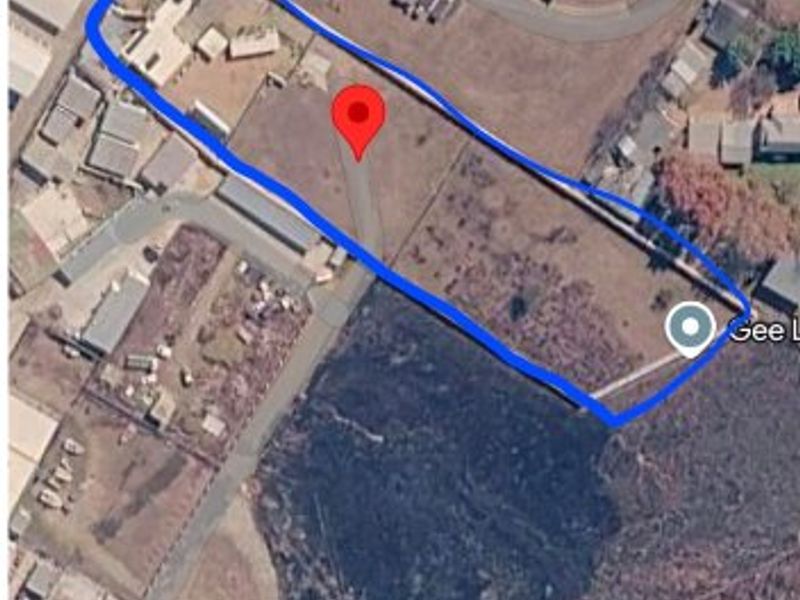 Aerial view of a commercial property plot with defined boundaries, showing existing structures and surrounding land access.