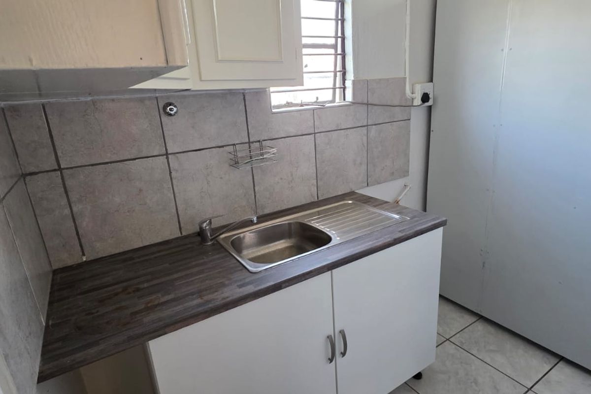 A compact kitchen area featuring a stainless steel sink, laminate countertop, tiled backsplash, and built-in cabinetry, suitable for a small commercial or office space.