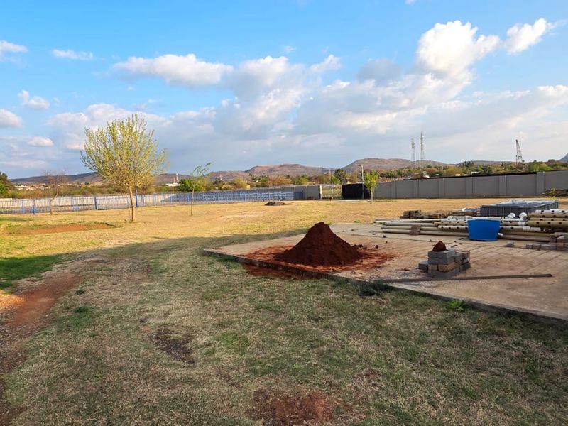 A large, undeveloped commercial garden area featuring a perimeter wall, concrete slab, and open lawn space with some construction materials present.