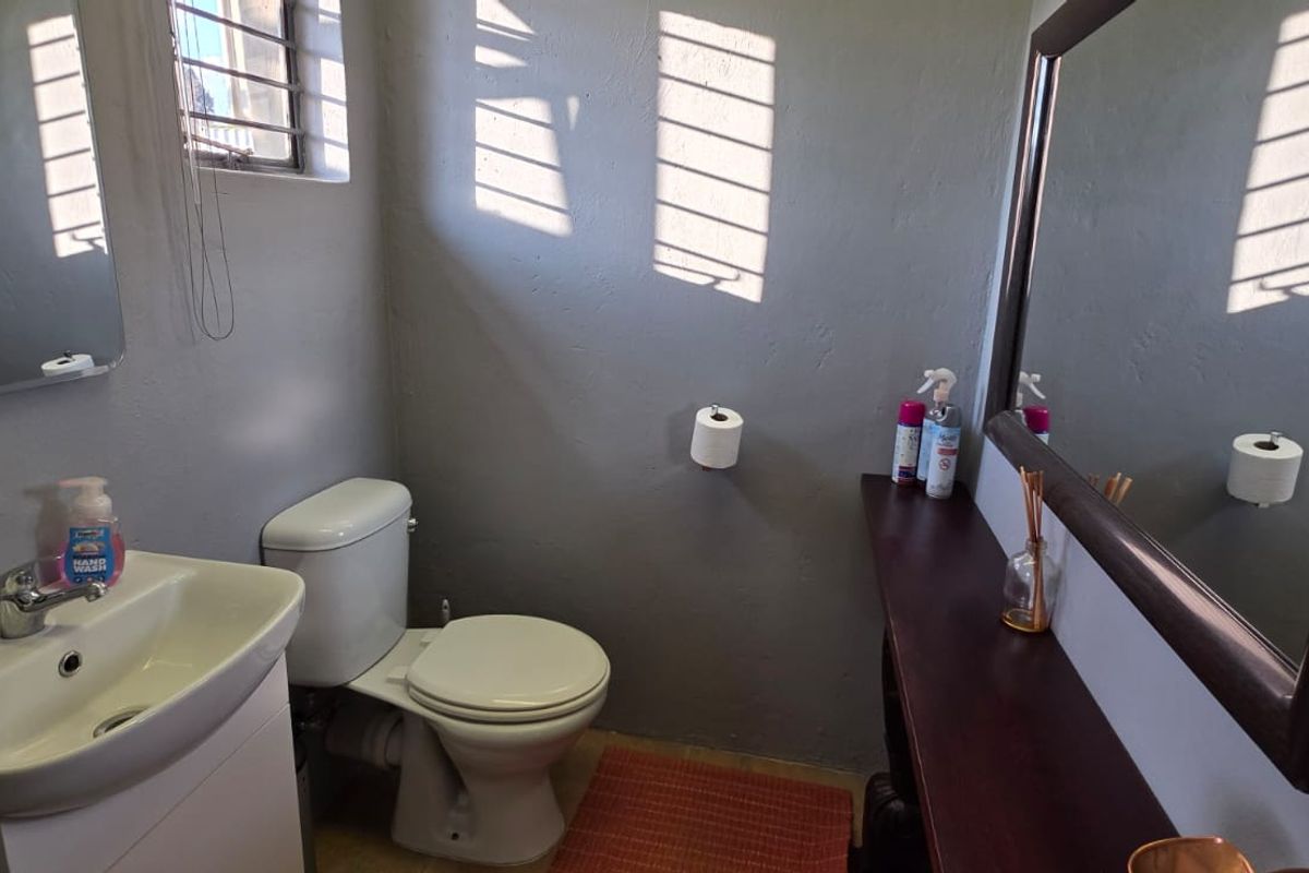 A functional bathroom featuring a vanity basin, toilet, and wall-mounted mirror, with natural light entering through a window with security bars.