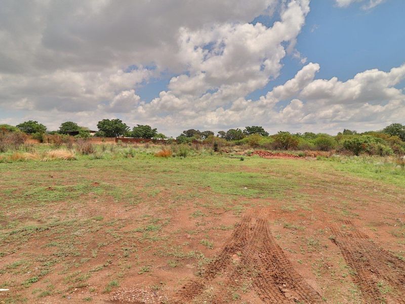A vacant residential plot featuring cleared ground, natural vegetation, and a perimeter wall, offering a blank canvas for future development.