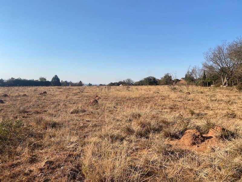 A wide-angle view of a vacant residential plot featuring natural dry grass and open landscape.