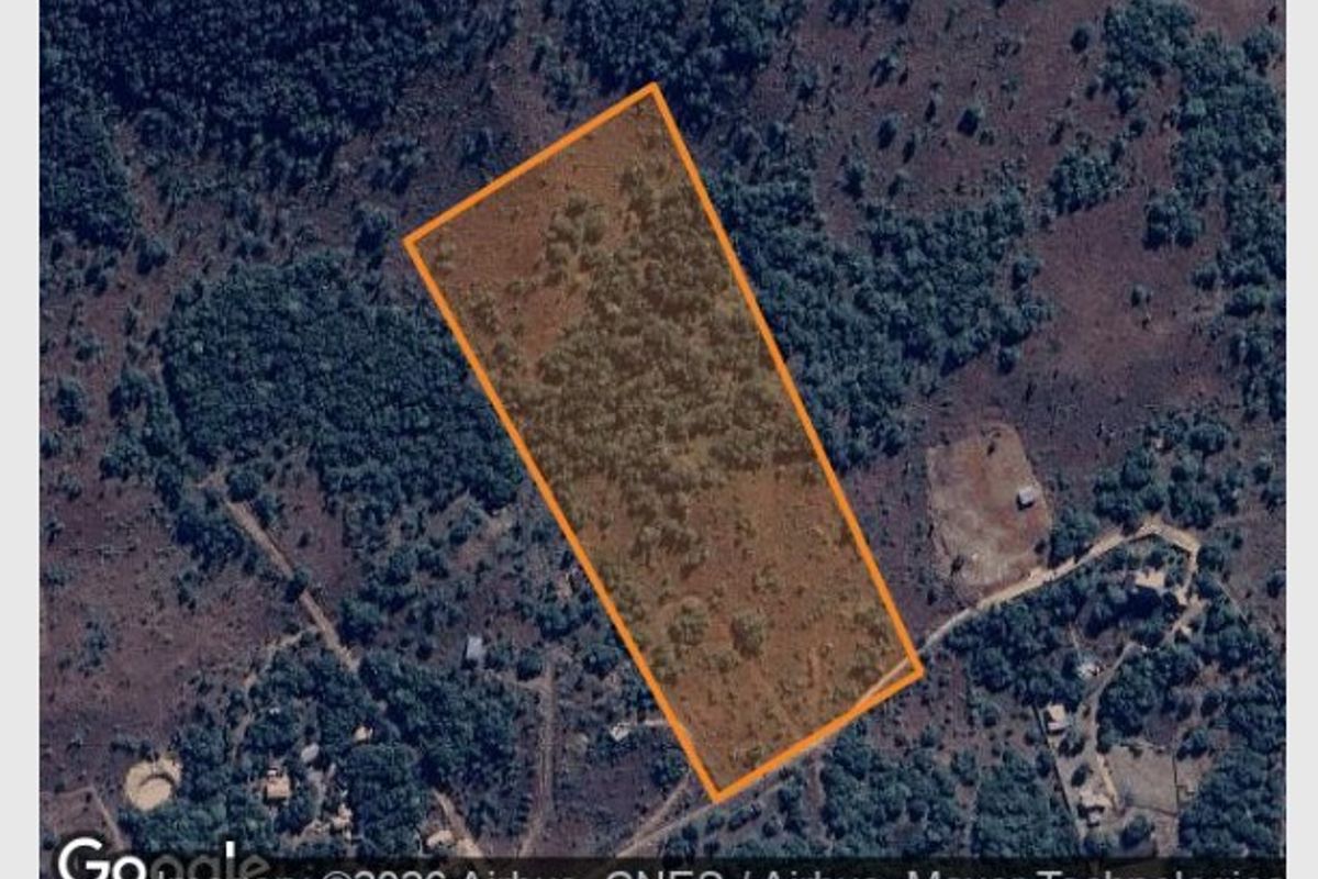 An aerial view of a vacant residential plot of land, highlighting the property boundaries and surrounding natural vegetation.