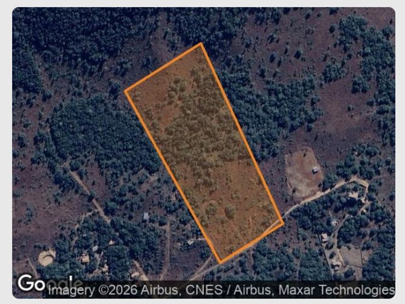 An aerial view of a vacant residential plot of land, highlighting the property boundaries and surrounding natural vegetation.