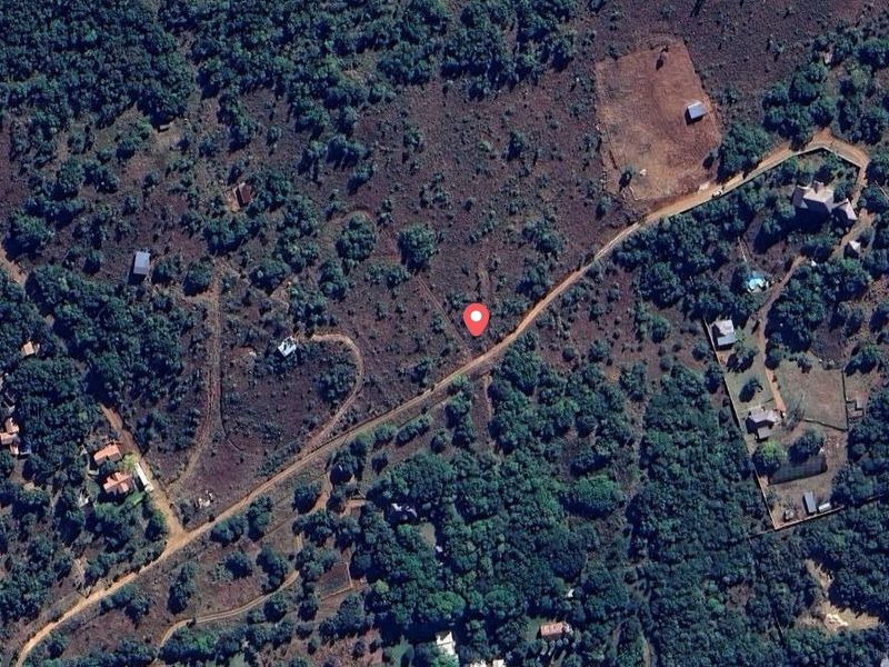 An aerial view of a vacant residential plot featuring native vegetation and access via a dirt road in a rural setting.