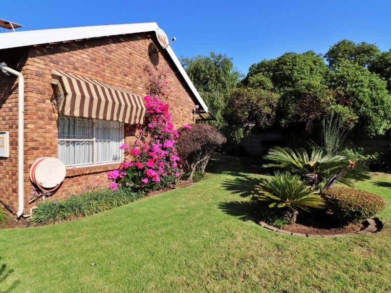 A well-maintained rear garden featuring a brick exterior wall, established landscaping, and a functional window awning.