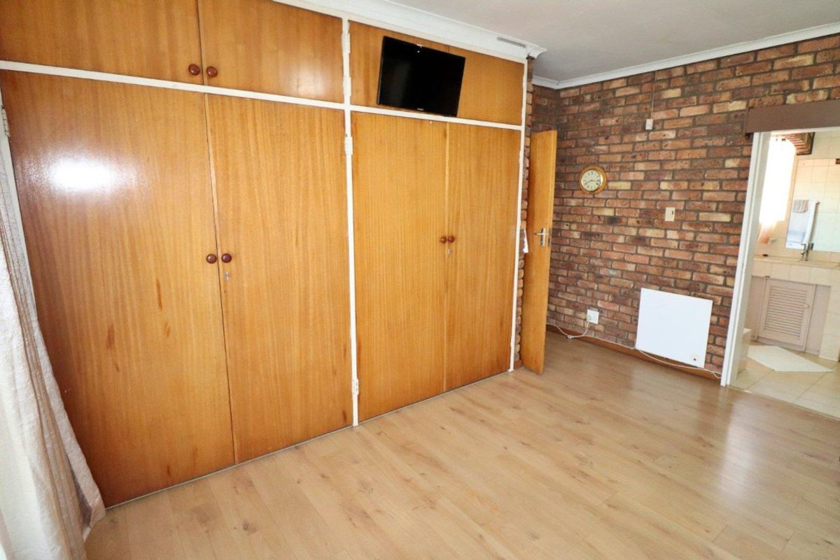 A bedroom featuring built-in wooden cupboards, an exposed brick feature wall, and laminate flooring, offering a functional space with potential for modern updates.