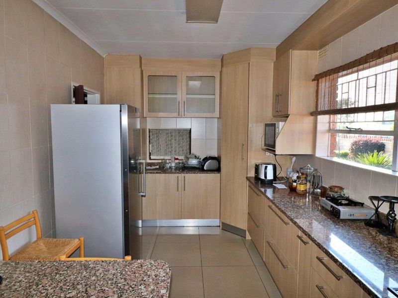 A functional kitchen featuring light wood cabinetry, granite countertops, tiled walls, and tiled flooring with ample storage space.