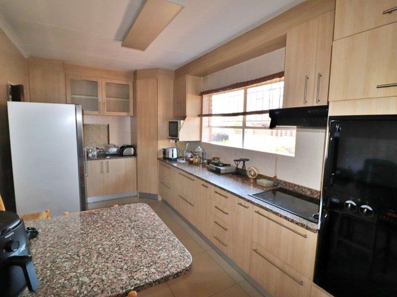 A functional kitchen featuring light wood cabinetry, granite countertops, a built-in oven, and an electric hob with an extractor fan.