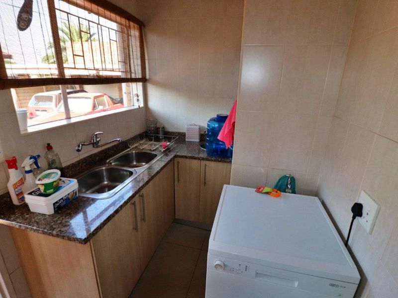 A functional laundry area featuring a double stainless steel sink, granite countertops, laminate cabinetry, and tiled finishes throughout.