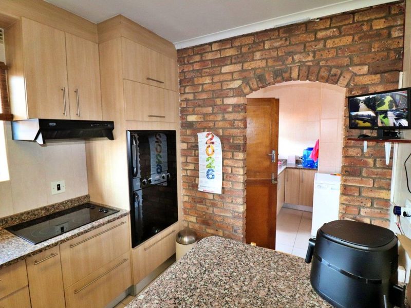 A functional kitchen featuring light wood cabinetry, granite countertops, an electric hob, and a distinctive exposed brick archway leading to an adjacent utility area.