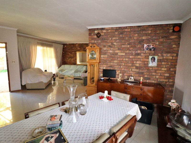 Spacious open-plan living and dining area featuring a prominent exposed brick wall, tiled flooring, and direct access to the outdoor patio.