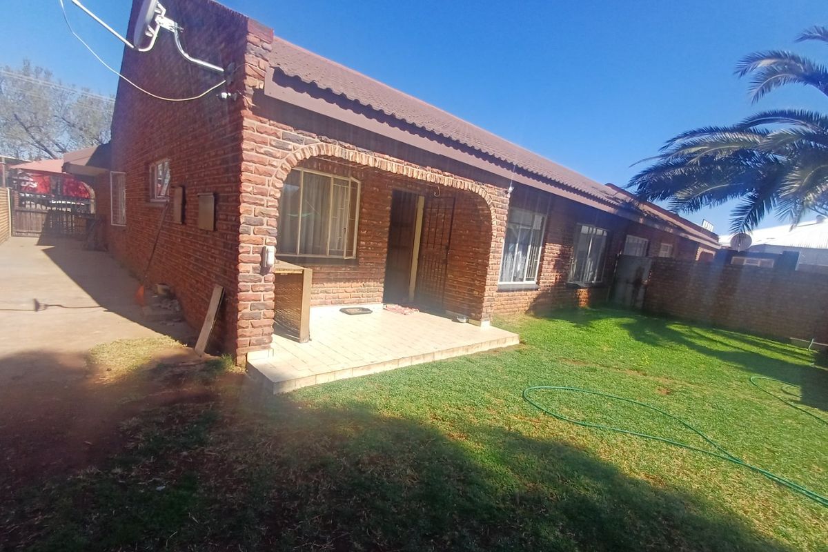 Rear view of a face brick house featuring a covered patio, arched architectural details, and a private garden area.