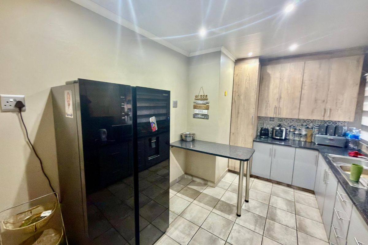 A functional kitchen featuring wood-look cabinetry, dark laminate countertops, a patterned tile backsplash, and tiled flooring with integrated lighting.