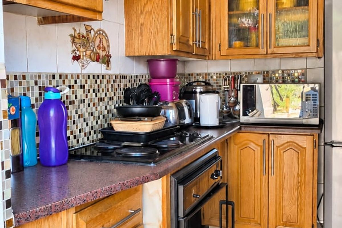 A dated kitchen featuring traditional wooden cabinetry, a built-in oven, electric hob, and tiled backsplash, offering potential for a modern renovation.