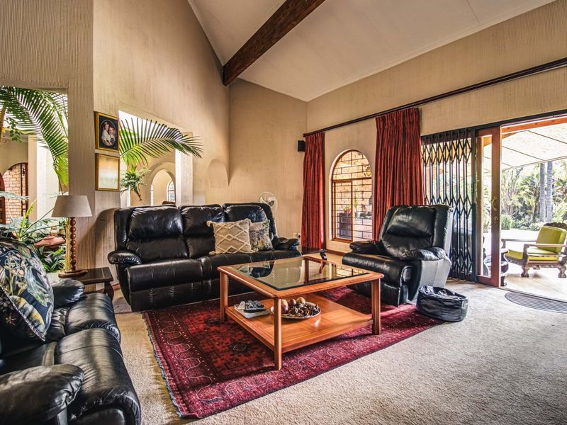 Spacious living room featuring a high vaulted ceiling with exposed timber beams, arched windows, and direct access to an outdoor patio area.