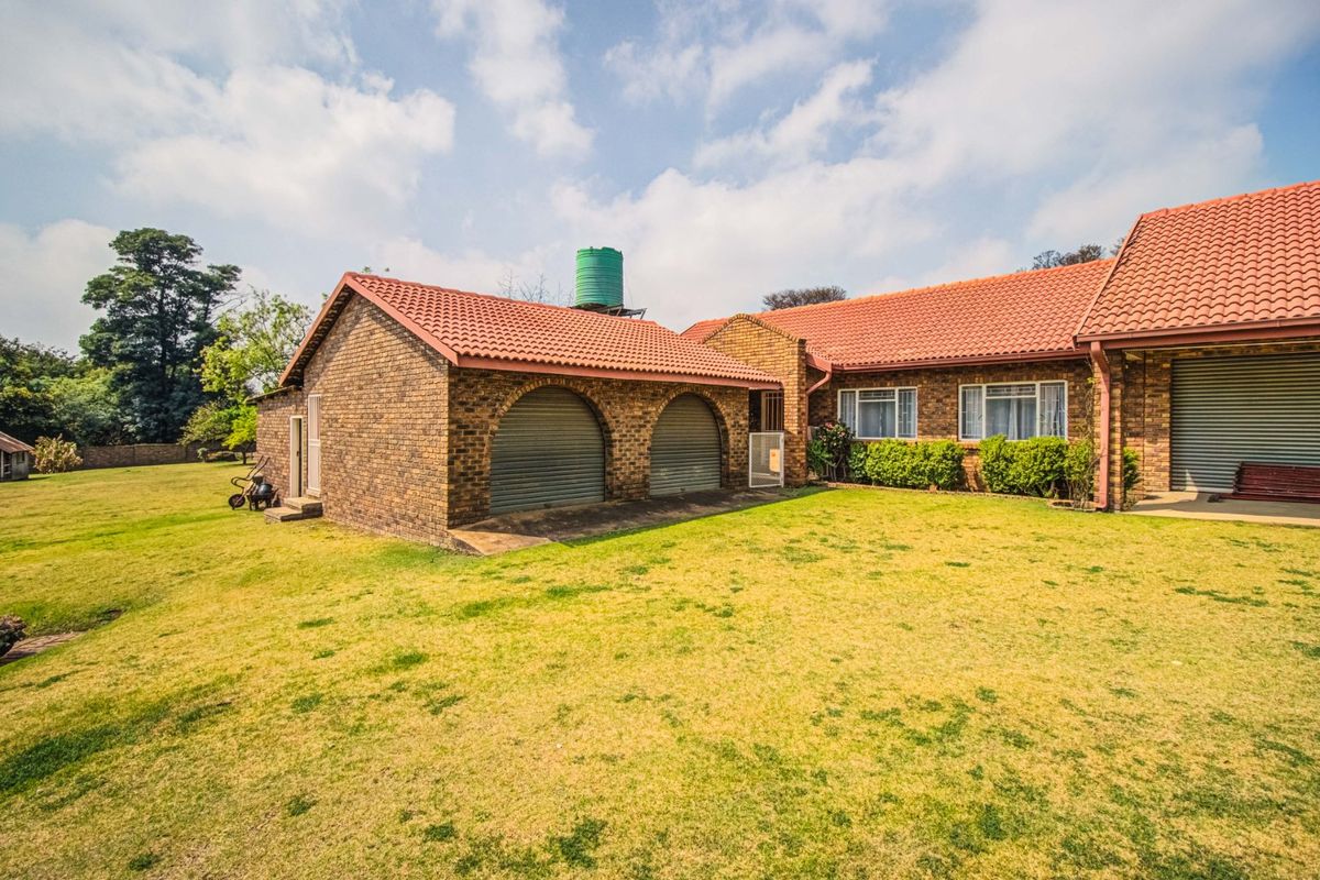 Rear view of a face brick farm property featuring a double garage with roller shutter doors and a large water storage tank.