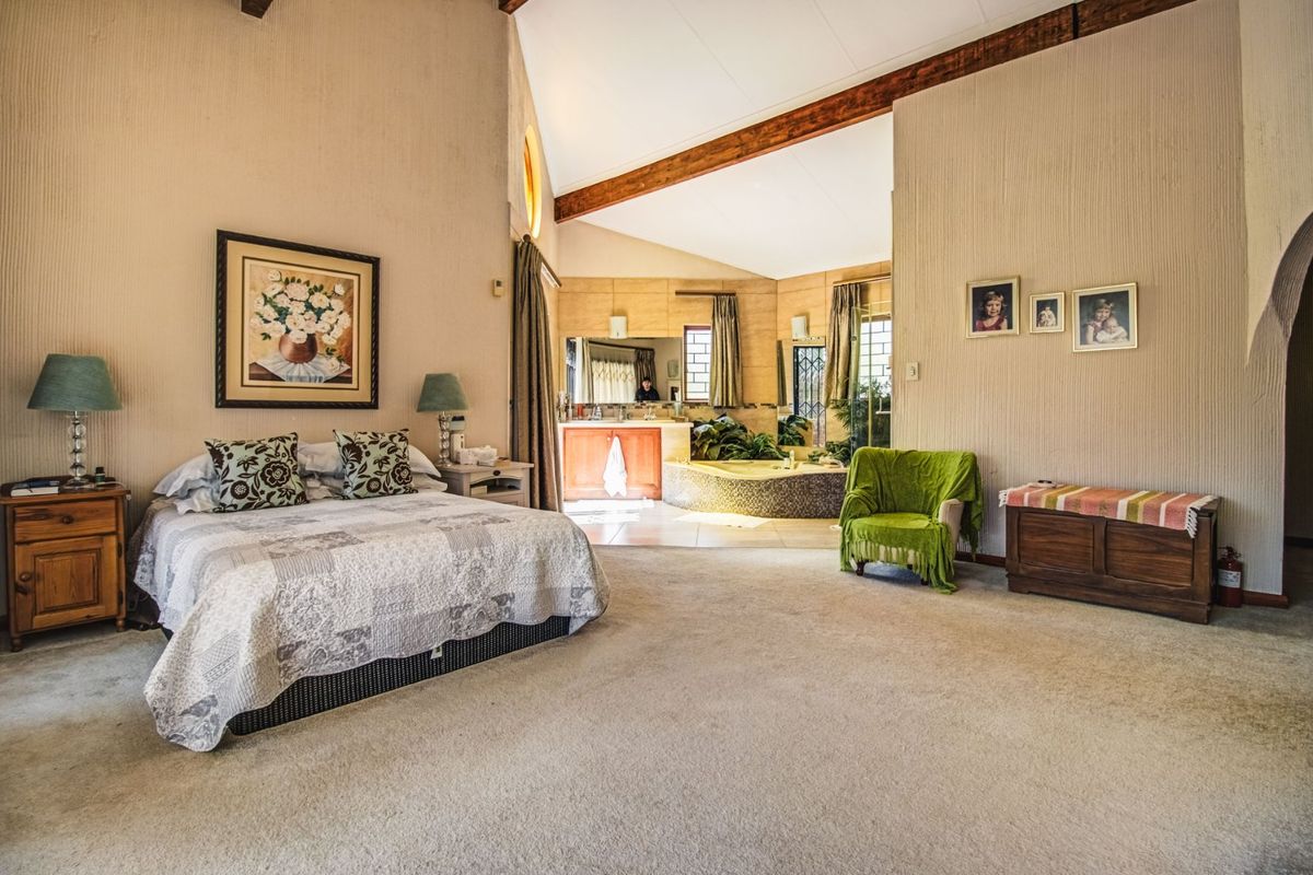Spacious bedroom featuring a vaulted ceiling with exposed timber beams and an open-plan en-suite bathroom with a built-in corner bathtub and vanity.