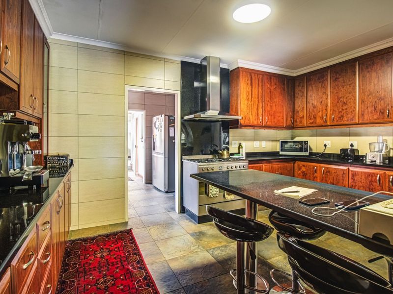 A well-maintained kitchen featuring rich wooden cabinetry, granite countertops, a stainless steel extractor fan, and a gas stove with a breakfast bar.