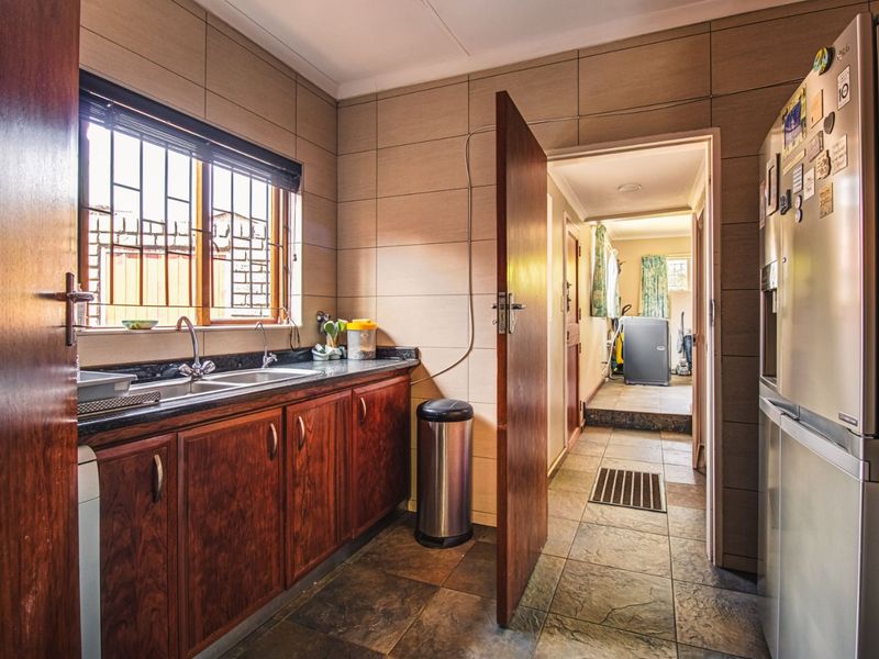 A functional scullery area featuring wooden cabinetry, granite countertops, a double sink, and tiled finishes, providing a practical space for food preparation and cleaning.