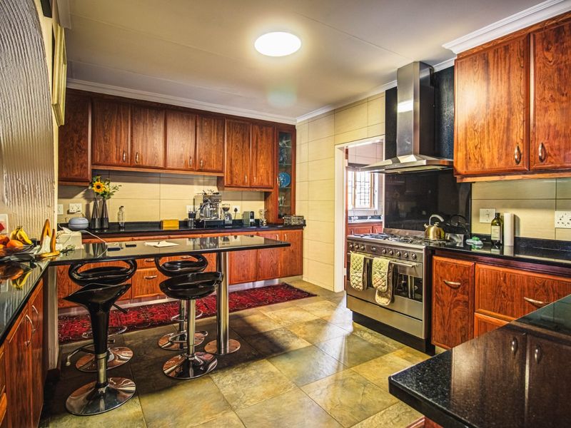 A well-maintained kitchen featuring rich wooden cabinetry, granite countertops, a stainless steel gas stove with extractor fan, and durable tiled flooring.