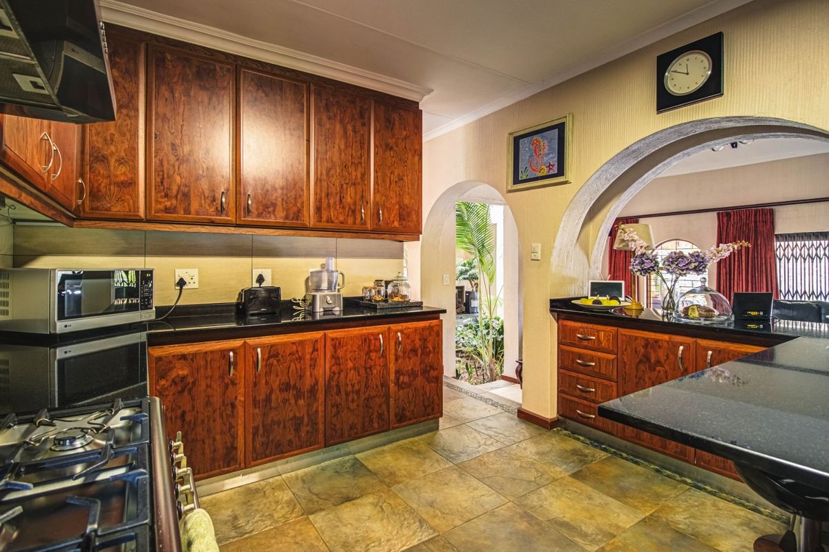 A well-maintained kitchen featuring rich wooden cabinetry, dark granite countertops, a gas stove with extractor fan, and a distinctive architectural archway.