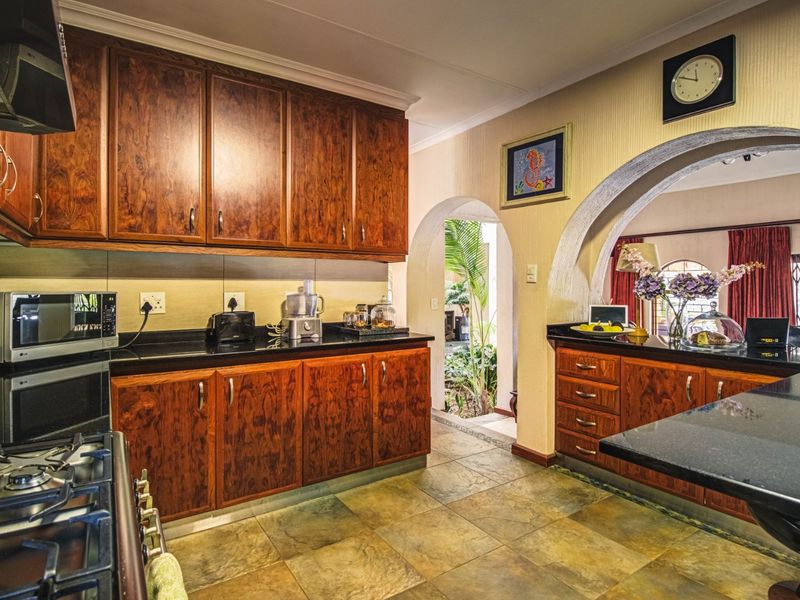 A well-maintained kitchen featuring rich wooden cabinetry, dark granite countertops, a gas stove with extractor fan, and a distinctive architectural archway.