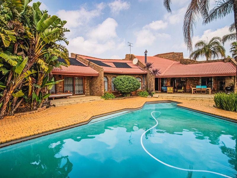 Spacious outdoor entertainment area featuring a swimming pool with solar heating, brick paving, and a covered patio attached to the main brick residence.