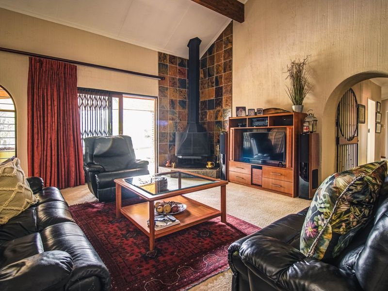 Spacious living room featuring a vaulted ceiling with exposed timber beam, a tiled fireplace surround with a freestanding fireplace, and arched architectural details.