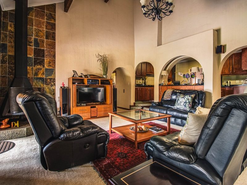 Spacious open-plan living area featuring a striking stone-clad fireplace, high vaulted ceilings with exposed beams, and arched transitions leading into the kitchen.