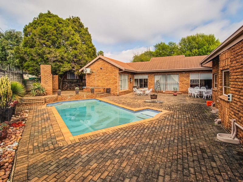 Outdoor entertainment area featuring a swimming pool, extensive brick paving, and a built-in brick fireplace, set against a face-brick house exterior.