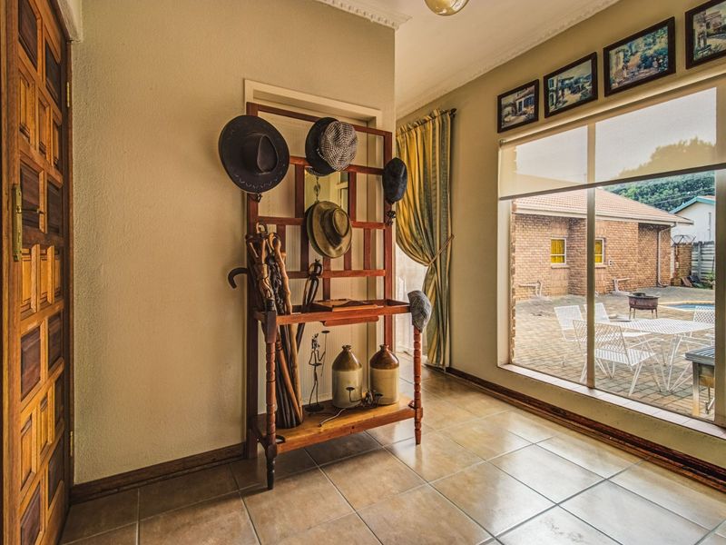 A bright entrance hall featuring tiled flooring, decorative cornicing, and a large window providing a view of the rear patio and garden area.