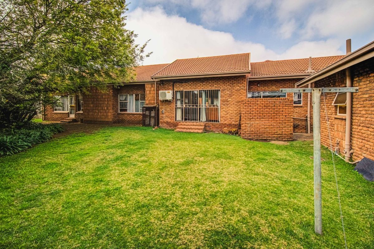 Rear view of a brick house featuring a tiled roof, sliding glass doors with security gates, an air conditioning unit, and a private garden.
