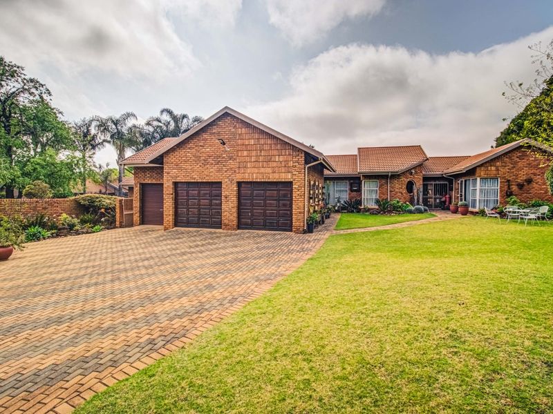 A well-maintained brick house featuring a double garage, expansive paved driveway, and a neatly landscaped front garden.