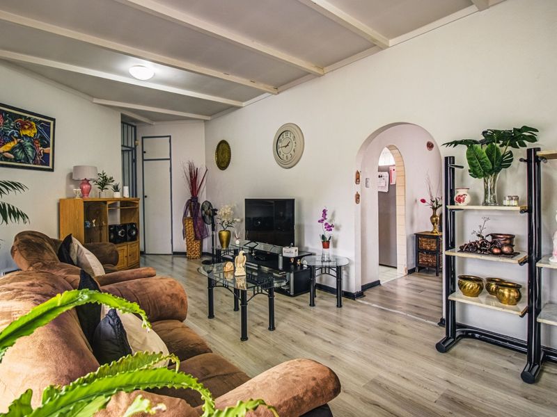A comfortable living room featuring laminate flooring, an arched doorway leading to adjacent spaces, and an exposed beam ceiling.