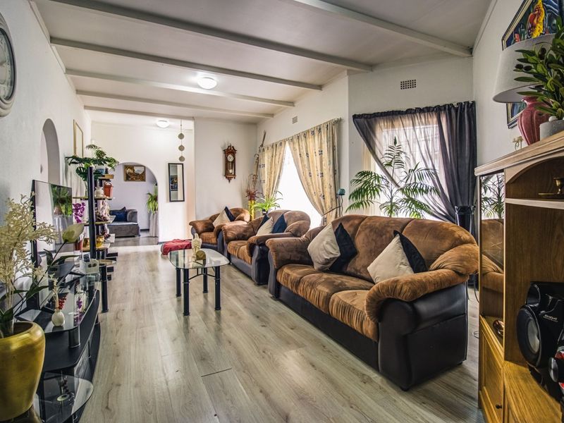 Spacious living room featuring light-toned laminate flooring, exposed beam ceilings, and a classic archway leading to adjacent living areas.