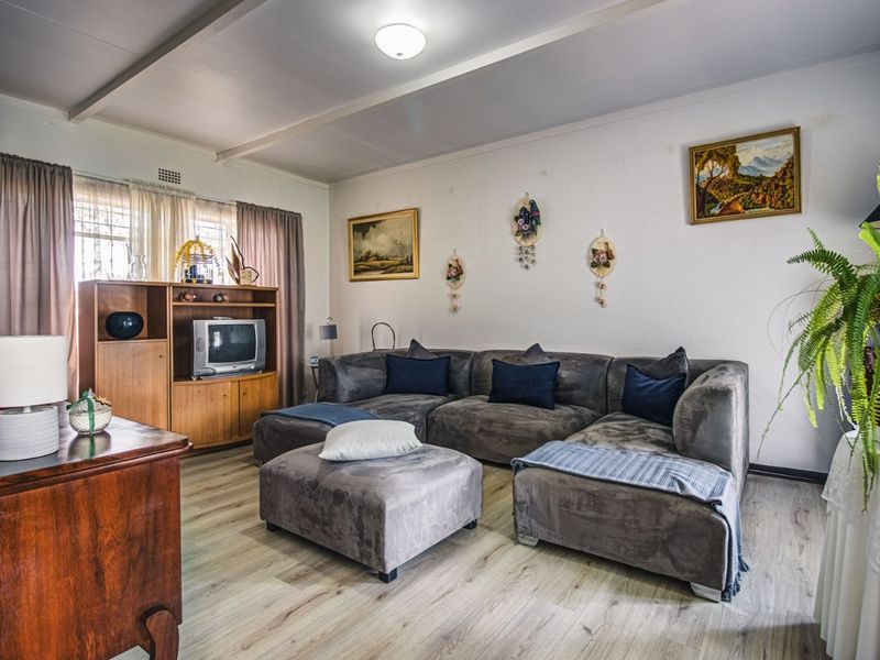 A comfortable living room featuring light-toned laminate flooring, neutral walls, and a window fitted with security bars.