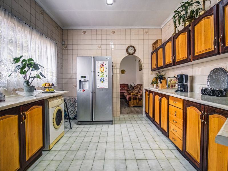A functional kitchen featuring traditional wooden cabinetry, tiled wall finishes, and tiled flooring, with an arched doorway leading to the adjacent living area.