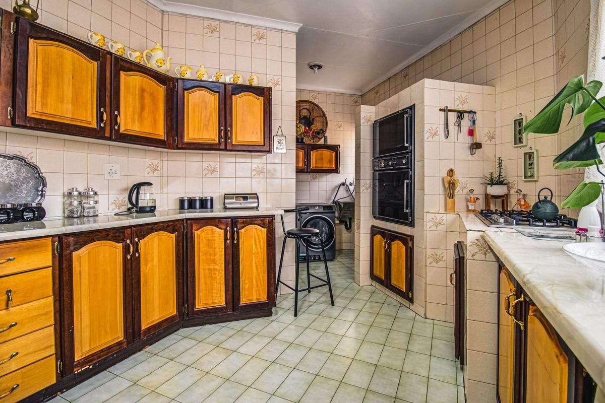 A functional kitchen featuring traditional wooden cabinetry, tiled splashbacks, built-in oven, and gas hob, with an adjacent laundry area.